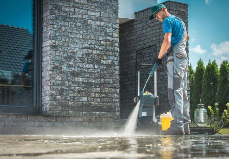 A man wearing overalls and apron cleaning a patio surface.